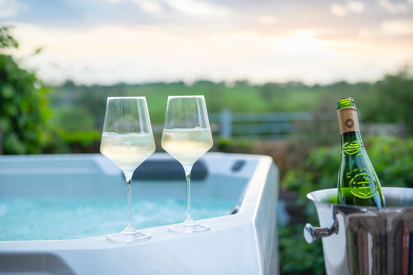 Two glasses and a bottle on ice at the edge of the hot tub at sunset