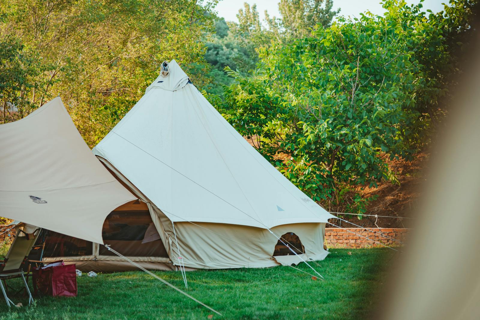 A cream canvas bell tent pitched on a green lawn with trees behind, ready for an overflow night