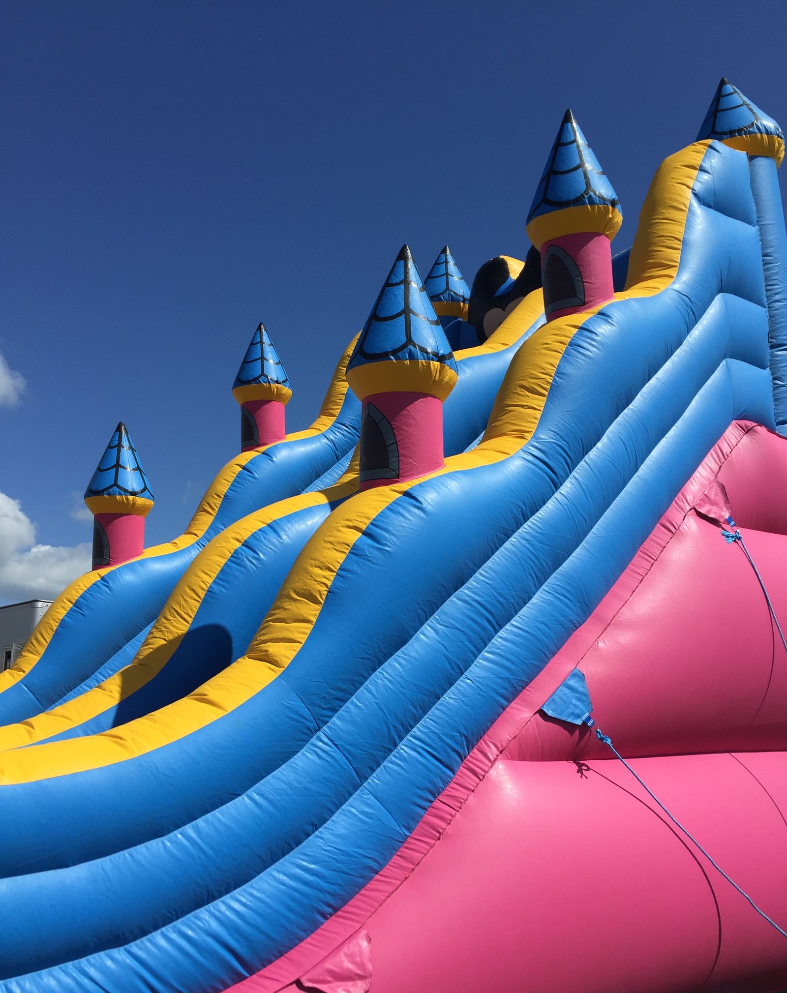 A bouncy castle with pink, blue and yellow turrets and slides set against a clear blue sky