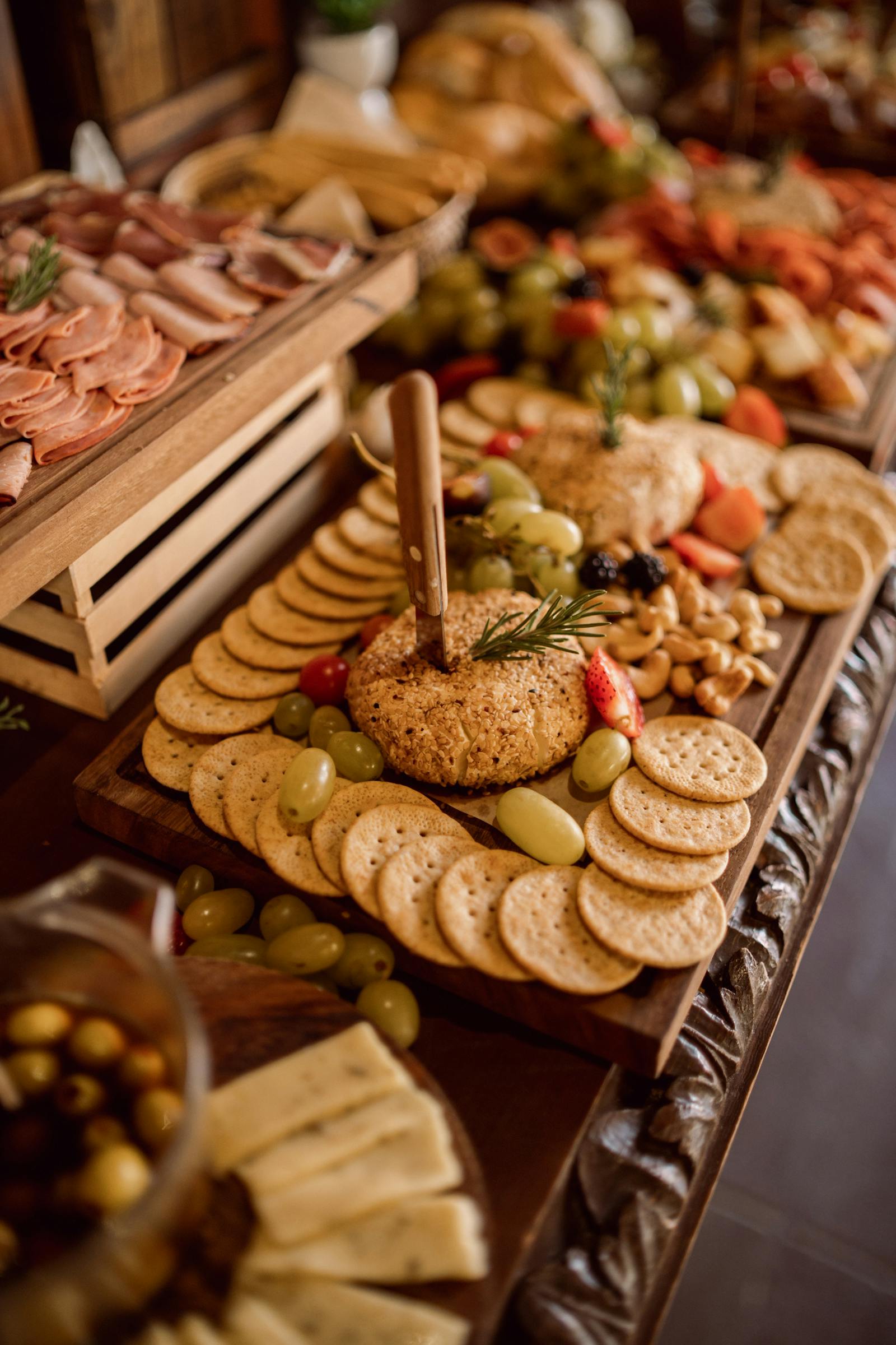 A grazing table spread of cheese, charcuterie, crackers, olives, grapes and dried fruit on wooden boards